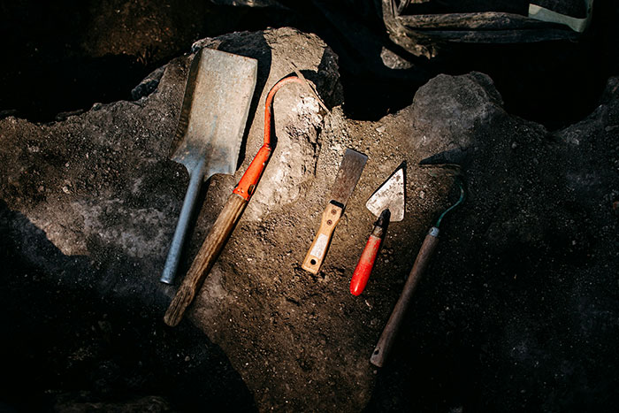 Various excavation tools arranged on soil at an archaeological job site highlighting real-life traps encountered by archaeologists