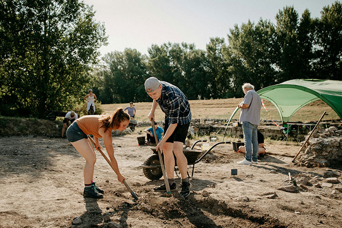Archaeologists carefully excavating a site outdoors with tools, uncovering potential traps and artifacts at a job site.