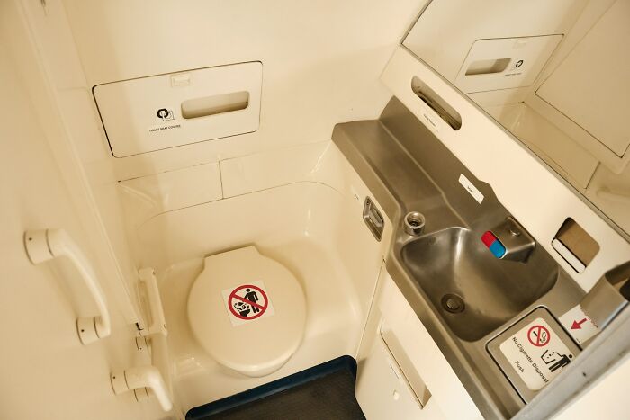 Compact airplane lavatory interior with toilet, sink, and safety signs highlighting underrated plane perks to utilize during flights.