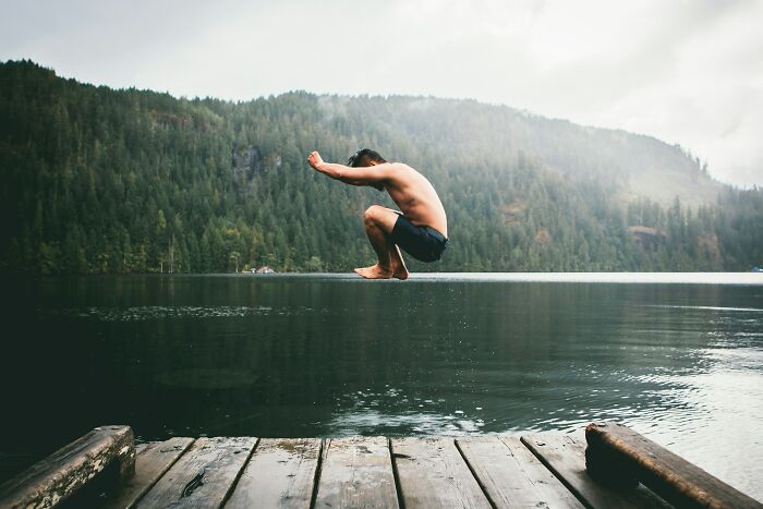 Person jumping into lake from wooden dock surrounded by forest, illustrating dangerous things often dismissed risks.