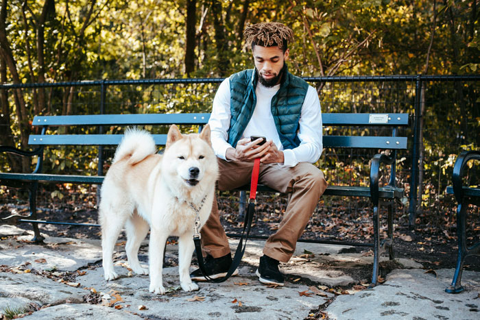 Man sitting on a park bench with his dog on a leash, illustrating dog owner and animal control interaction.