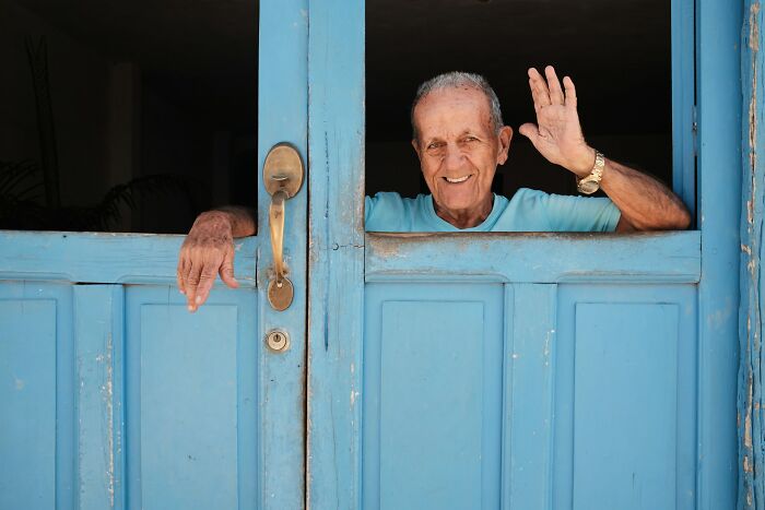 Elderly man smiling and waving through a bright blue door, evoking feelings of strange things people witnessed.
