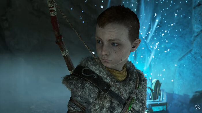 Atreus from God of War video game, wearing fur armor and holding a bow in a mystical blue-lit cave scene.