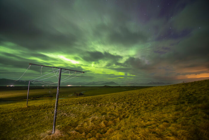 Aurora borealis lighting up the night sky over a rural field with old wooden poles, inspiring strange things witnessed.
