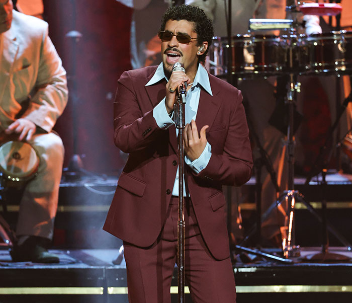 Bad Bunny performing on stage in a maroon suit and sunglasses highlighting his immaculate transformation after Grammy win