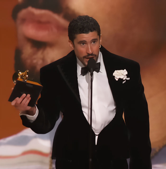 Man in tuxedo holding Grammy award on stage, highlighting Bad Bunny's immaculate transformation after historic win.