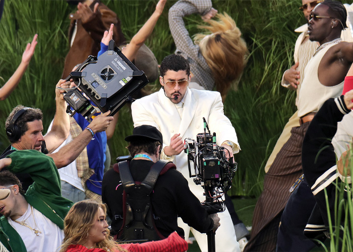 Performer in white suit dancing during Super Bowl 2026 halftime show amid camera crew and energetic crowd.