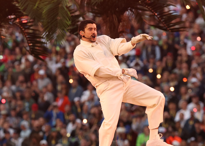 Performer in white outfit dancing during Super Bowl 2026 halftime show with audience in the background.