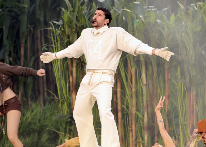 Performer wearing white outfit on stage with dancers and greenery in the background during Super Bowl 2026 halftime show.