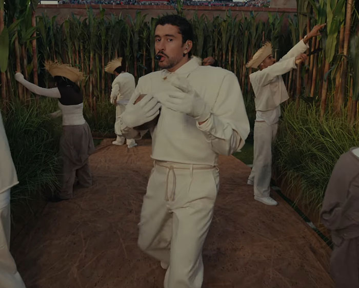 Bad Bunny performing in white outfit with dancers in cornfield setting, sparking debate after fans translate his explicit lyrics.