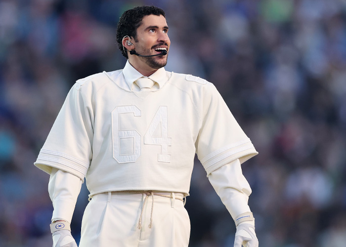 Bad Bunny performing at the Super Bowl 2026 halftime show, wearing a white outfit with number 64 on stage.