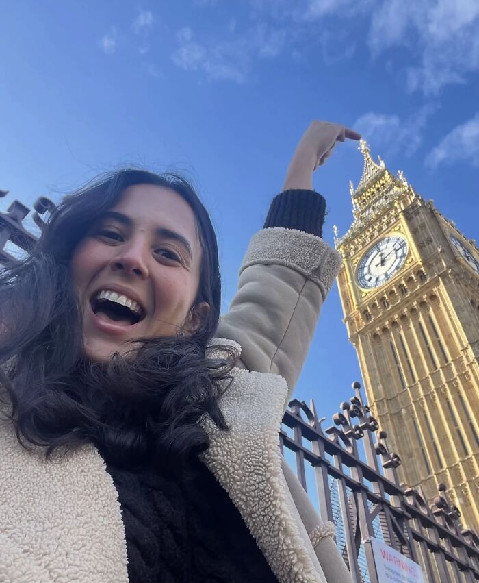Happy woman taking a chaotic energy mom selfie in front of Big Ben on a clear sunny day in London.