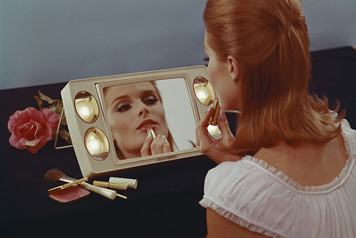 Woman applying lipstick while looking in mirror, highlighting beauty standards and their impact on women. Woman applying lipstick while looking in mirror, highlighting beauty standards and their impact on women.