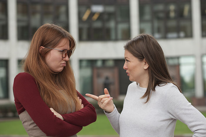 Two women outside, one upset with arms crossed, the other pointing and talking about best friend backup plan hurt issues.