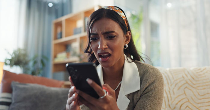 Woman reacting with shock while looking at her phone, illustrating a man spinning a tale about pregnant female bestie.