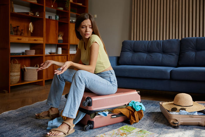 Woman sitting on an overstuffed suitcase, looking confused and frustrated, representing a tale about a pregnant female bestie.