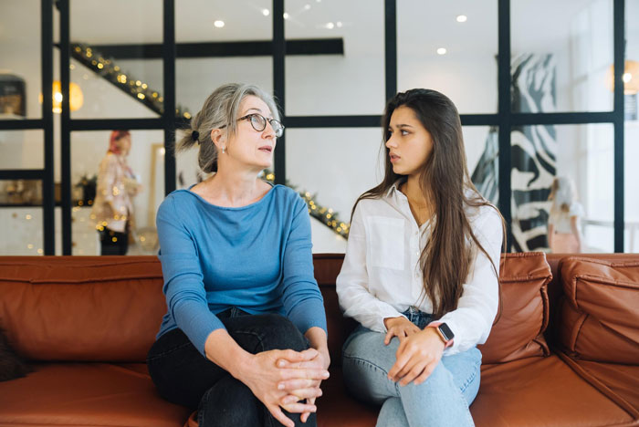 Two women sitting on a couch having a serious conversation about a pregnant female bestie in a modern living room.
