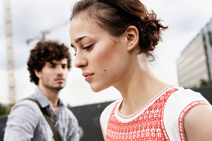 Young woman looking upset in foreground with young man in background, highlighting tensions in maid of honor duties at wedding.