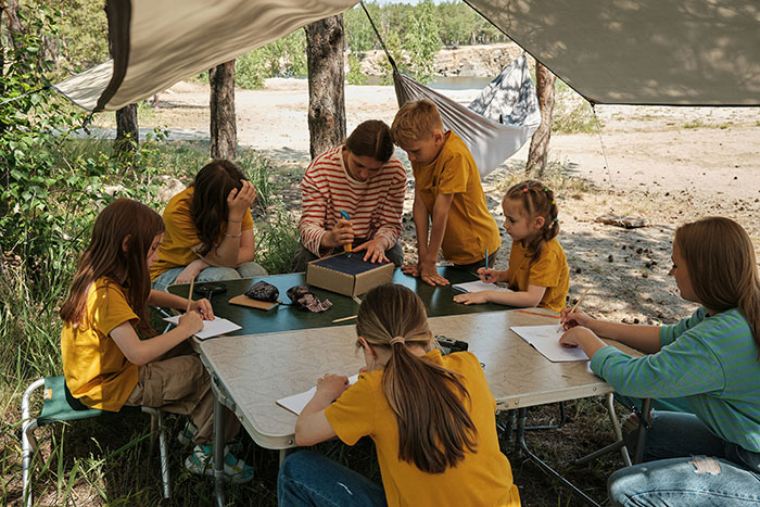 Group of children and a teacher outdoors under a canopy solving infamous unsolved mysteries with focused expressions.