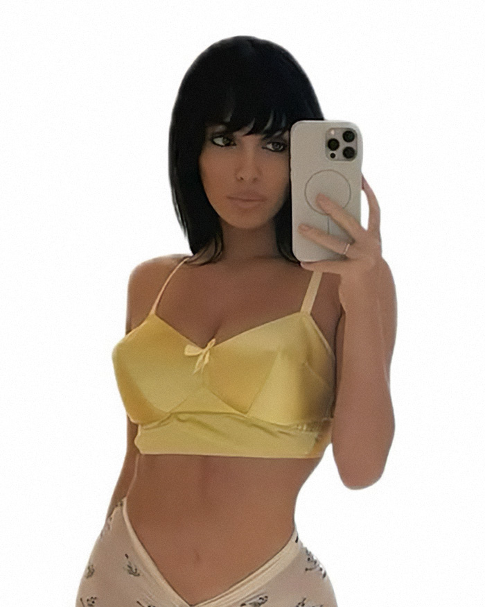 Bianca Censori taking a mirror selfie in a yellow crop top and light patterned pants showcasing bold outfits style.