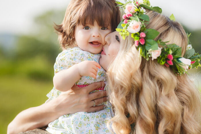 Woman with flower crown holding and kissing a toddler, illustrating tender moments in stories about first dates and encounters.