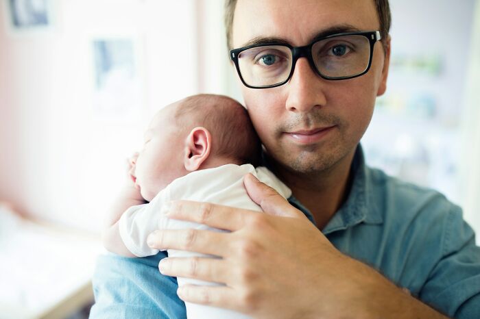 Man wearing glasses holding a baby close, portraying tender moments and emotional first encounters on a personal level.