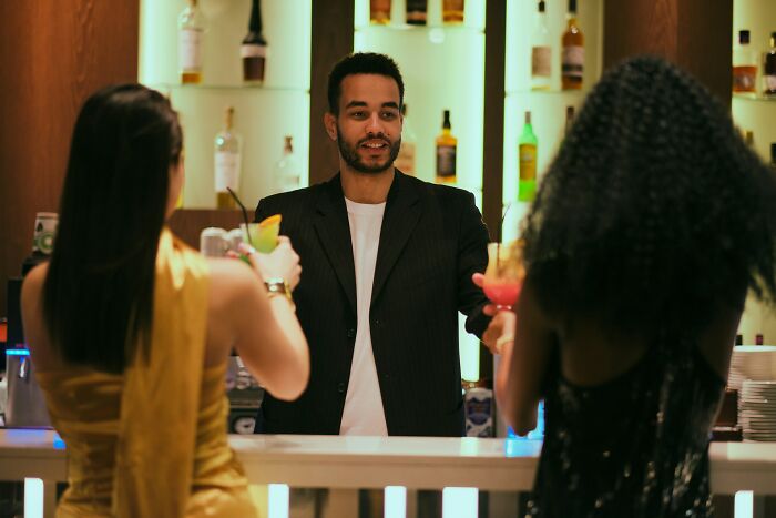 Bartender serving drinks to two women at a bar during a night out, capturing first dates and encounters mortified moments.