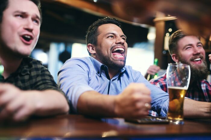 Three men laughing and cheering at a bar, capturing moments from first dates and encounters that left people mortified.