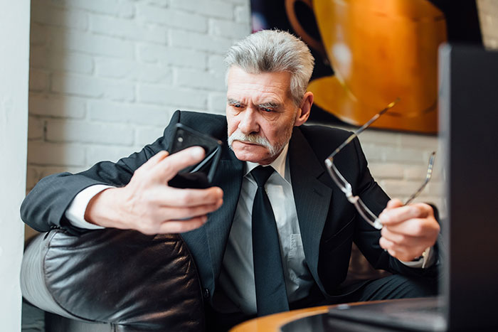 Older man in a suit looking shocked at his phone, reflecting on drunk confessions and unexpected life revelations.