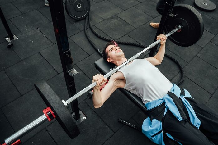 Young man bench pressing weights at the gym, focused on strength training during his intense workout session.