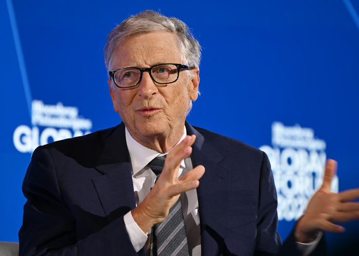 Bill Gates speaking at a conference, wearing glasses and a dark suit, related to Epstein Files and alleged STD claims.