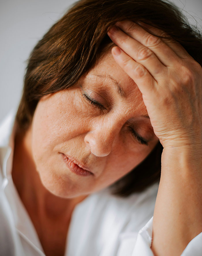 Woman with tired expression holding head in hand, illustrating a contrast to weirdly hilarious images to improve mood.