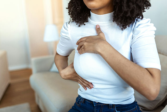 Woman sitting on a couch wearing white shirt, holding her chest and ribs in a weirdly hilarious moment to improve mood.