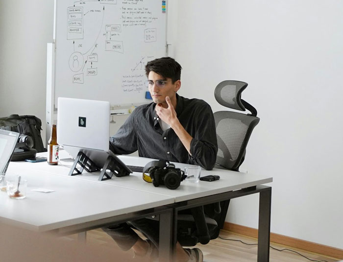 Young man working at a desk, reflecting thoughtfully on his laptop in a modern office, addressing low weight comments.