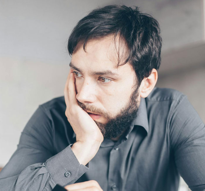 Man with beard looking thoughtful, resting his face on hand, reflecting on comments about his low weight from boss.