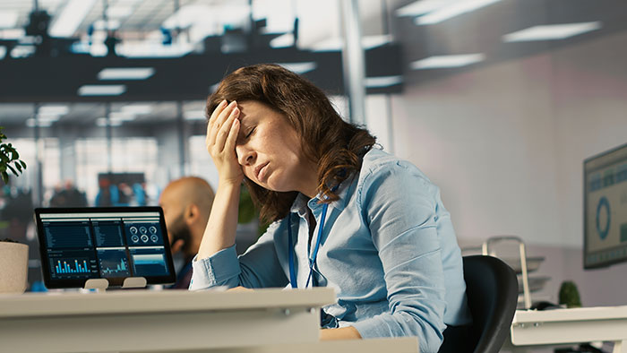 Person disappointed in boss they looked up to, sitting at desk with hand on forehead in modern office setting.