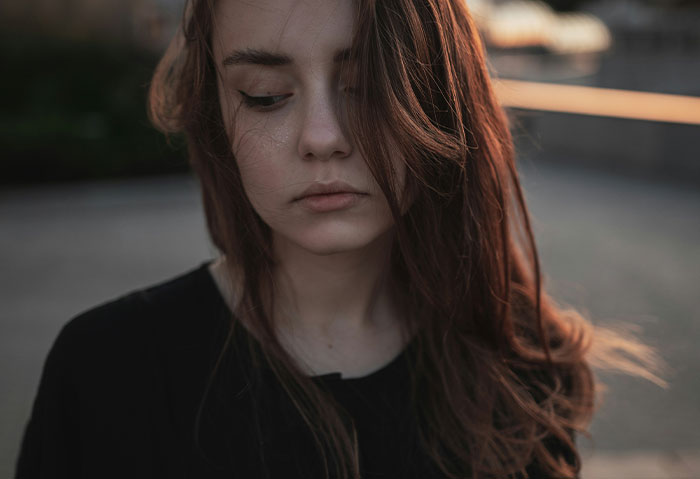 Young woman with long hair looking down thoughtfully, portraying confusion over cheating confession and boyfriend's denial.