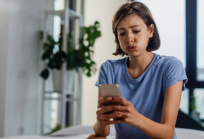 Young woman looking worried while holding phone, facing confusion over cheating confession and boyfriend's denial.