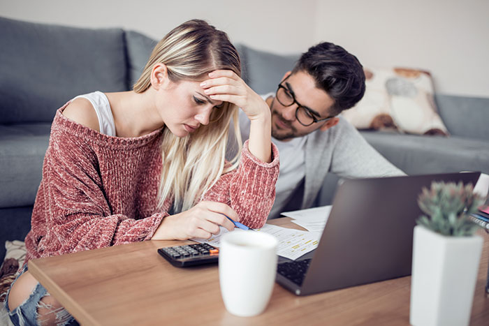 Couple reviewing finances at home, woman looking stressed while man watches, focusing on financial challenges together.