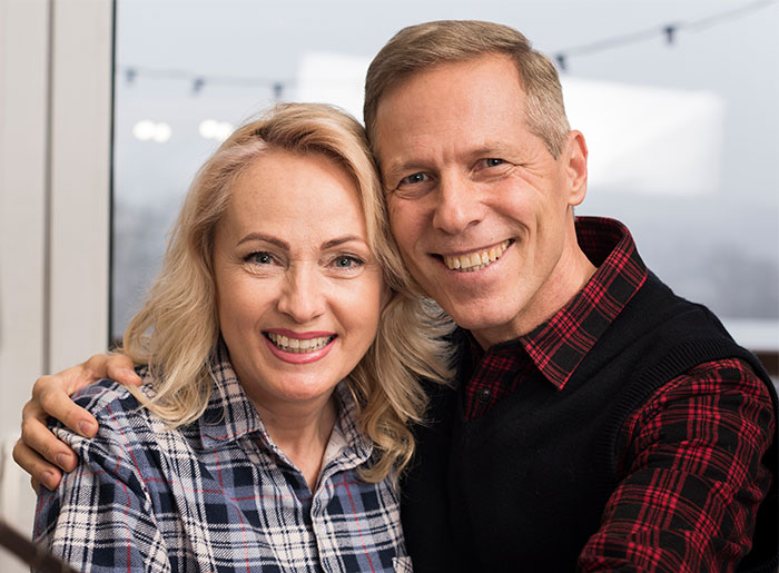 Smiling middle-aged couple in cozy plaid shirts shares a warm moment, highlighting new grandma drama and boyfriend breakup themes.