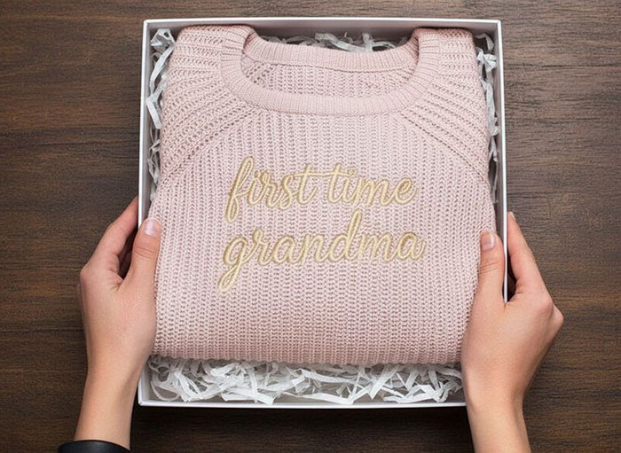 Pink knitted sweater folded in a box with gold embroidery first time grandma held by hands for boyfriend breakup new grandma drama.