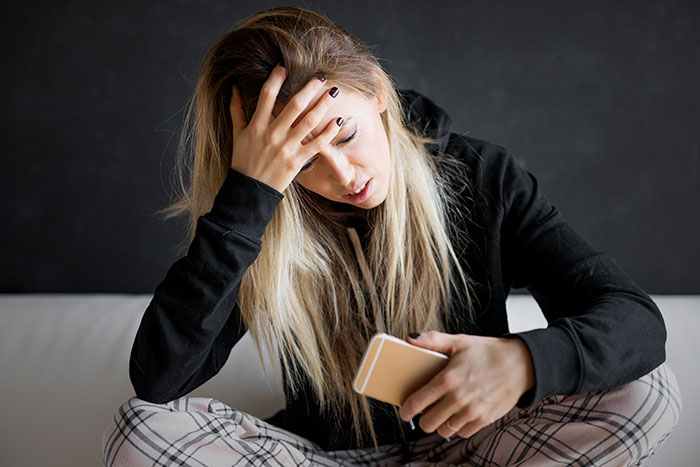 Young woman looking horrified and stressed while holding her phone, reflecting boyfriend abandoning her on date night.