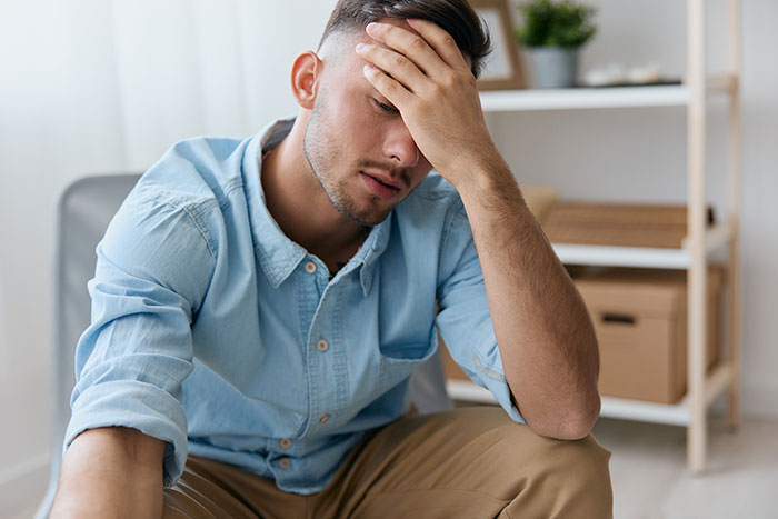 Young man in a blue shirt sitting with hand on forehead, appearing upset after a disagreement at a restaurant.