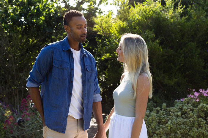 Man with casual denim shirt talking to smiling woman in garden, illustrating cheater with 9 kids and baby mamas concept