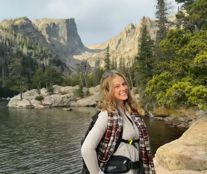 Young woman hiking New York's highest peak near a lake, surrounded by trees and rocky mountain landscape.