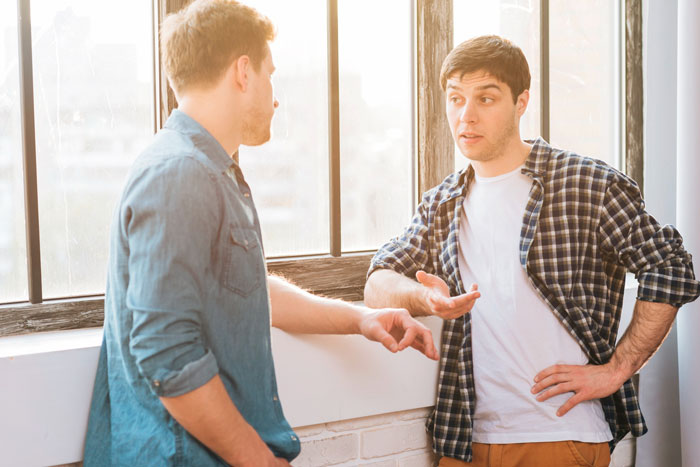 Two men talking by a window, one handing a rent bill as veteran pay increases trigger a money-focused reaction.