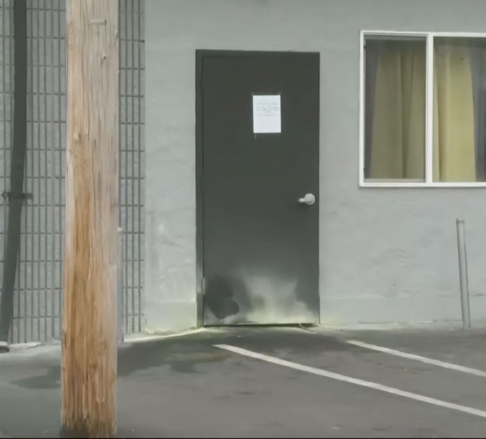 Black metal door on gray building exterior with parking lines and wooden utility pole near entrance, related to criminal history news. Black metal door on gray building exterior with parking lines and wooden utility pole near entrance, related to criminal history news.