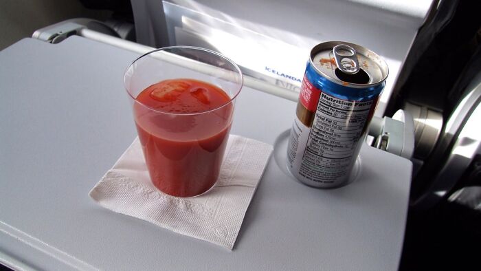 Plastic cup of tomato juice and a soft drink can on an airplane tray table showcasing underrated plane perks.