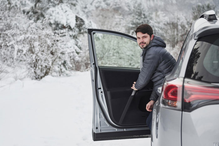 Man in a winter jacket opening car door in snowy parking lot, frustrated about snow-free parking spot dispute. Man in a winter jacket opening car door in snowy parking lot, frustrated about snow-free parking spot dispute.