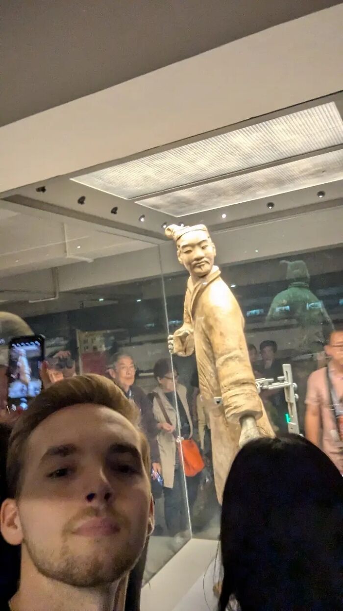 Young man taking a humorous selfie in front of a historic statue, capturing chaotic energy and selfie moments on social media.